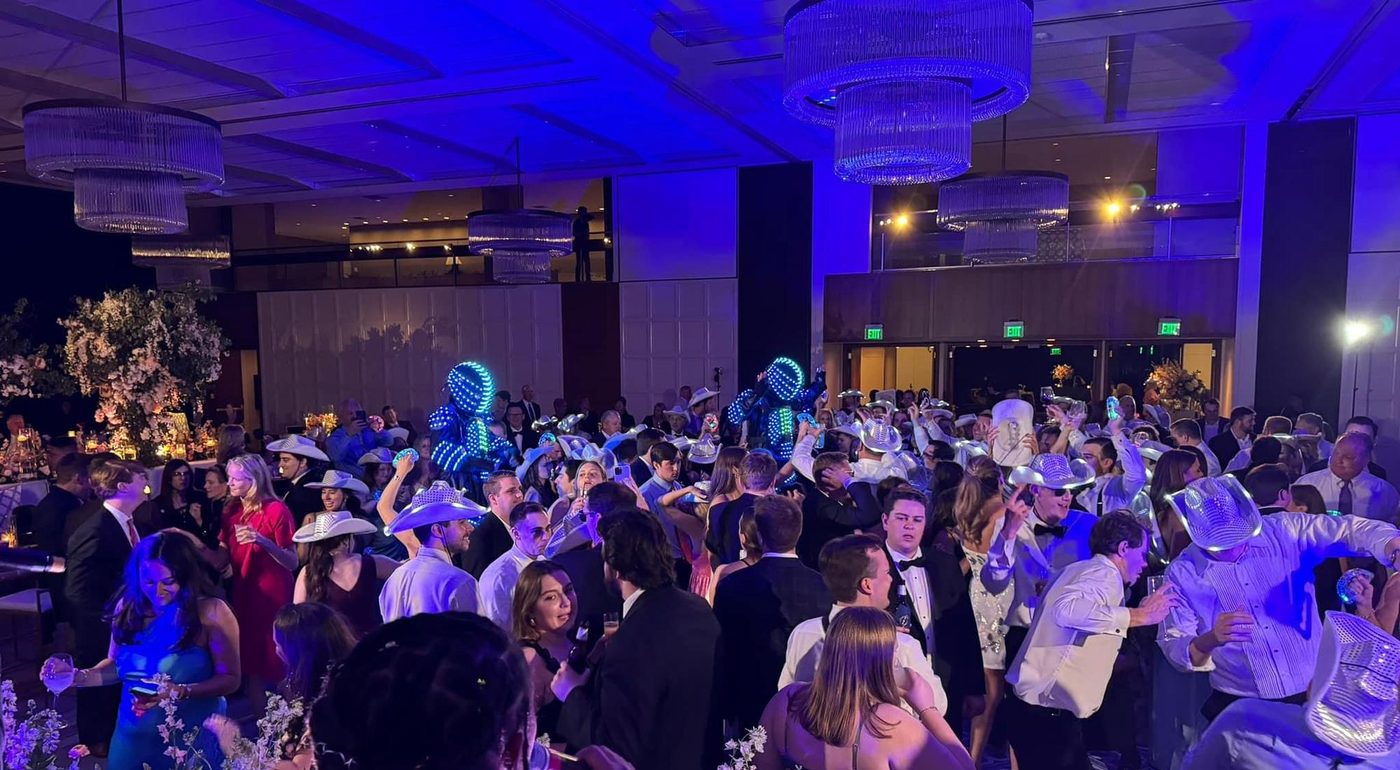 A packed gala ballroom washed in blue light, guests in formal wear dancing under chandeliers.