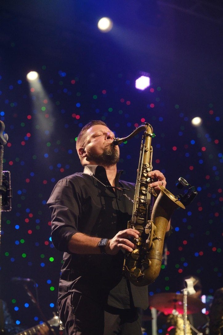 A saxophonist playing a solo under stage lights and haze.