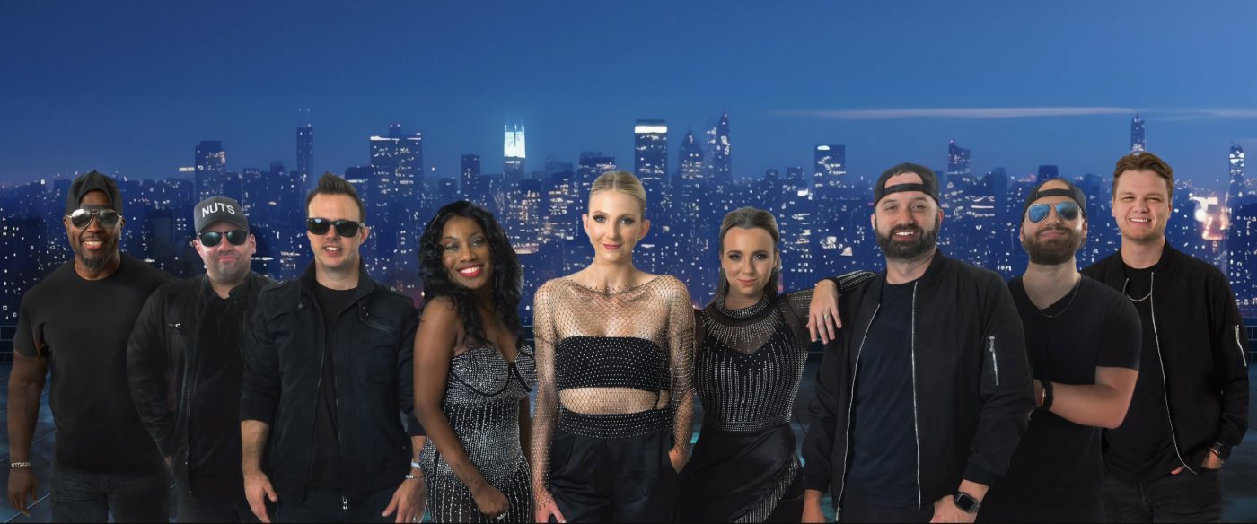 The Mixed Nuts — nine band members in black stage wear, posed in a line in front of a night-time city skyline.